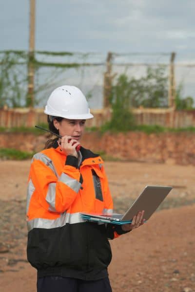 Land surveyor in safety gear using a laptop to verify boundary survey data and ensure property line accuracy