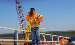 Surveyor using a total station as part of a construction staking survey at an active construction site