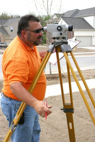 Flood elevation survey shown by a land surveyor using tripod equipment to measure property elevations
