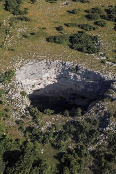  Aerial view of a large sinkhole collapse in a rocky grassy landscape showing why a topographic survey is essential for identifying land risks

