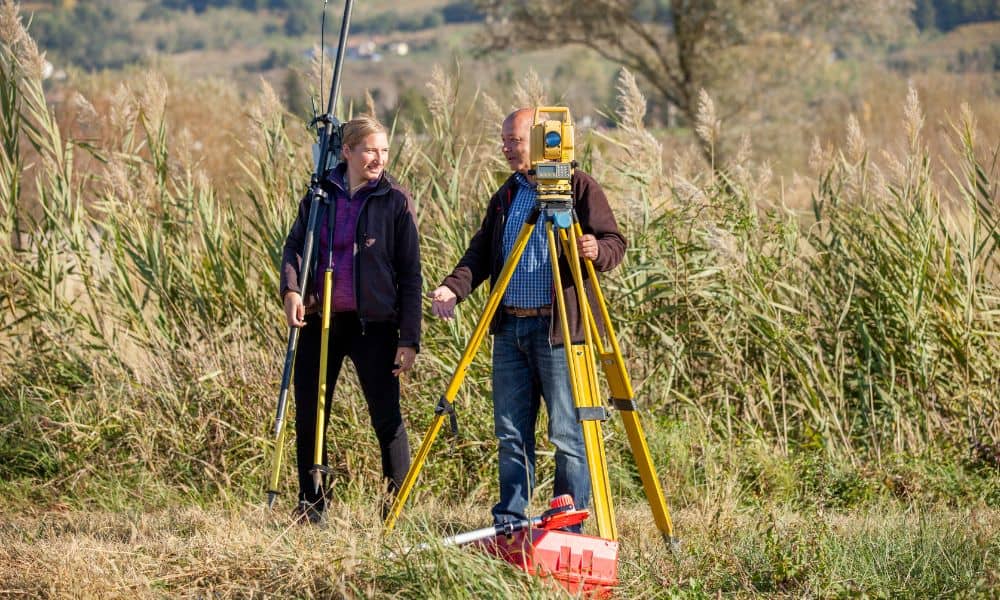 Two land surveyors using total station and GPS equipment during a topographic survey in an open field
