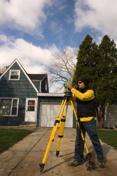 Land surveyor measuring elevation at a residential property to prepare a FEMA elevation certificate for flood risk and insurance purposes